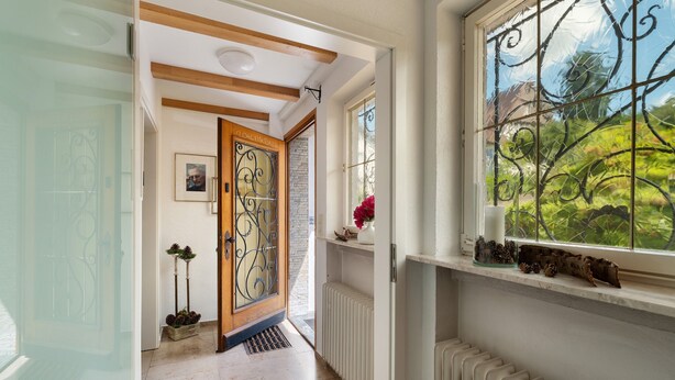 Un couloir avec une porte en bois, un radiateur et une fenêtre donnant sur un paysage verdoyant.