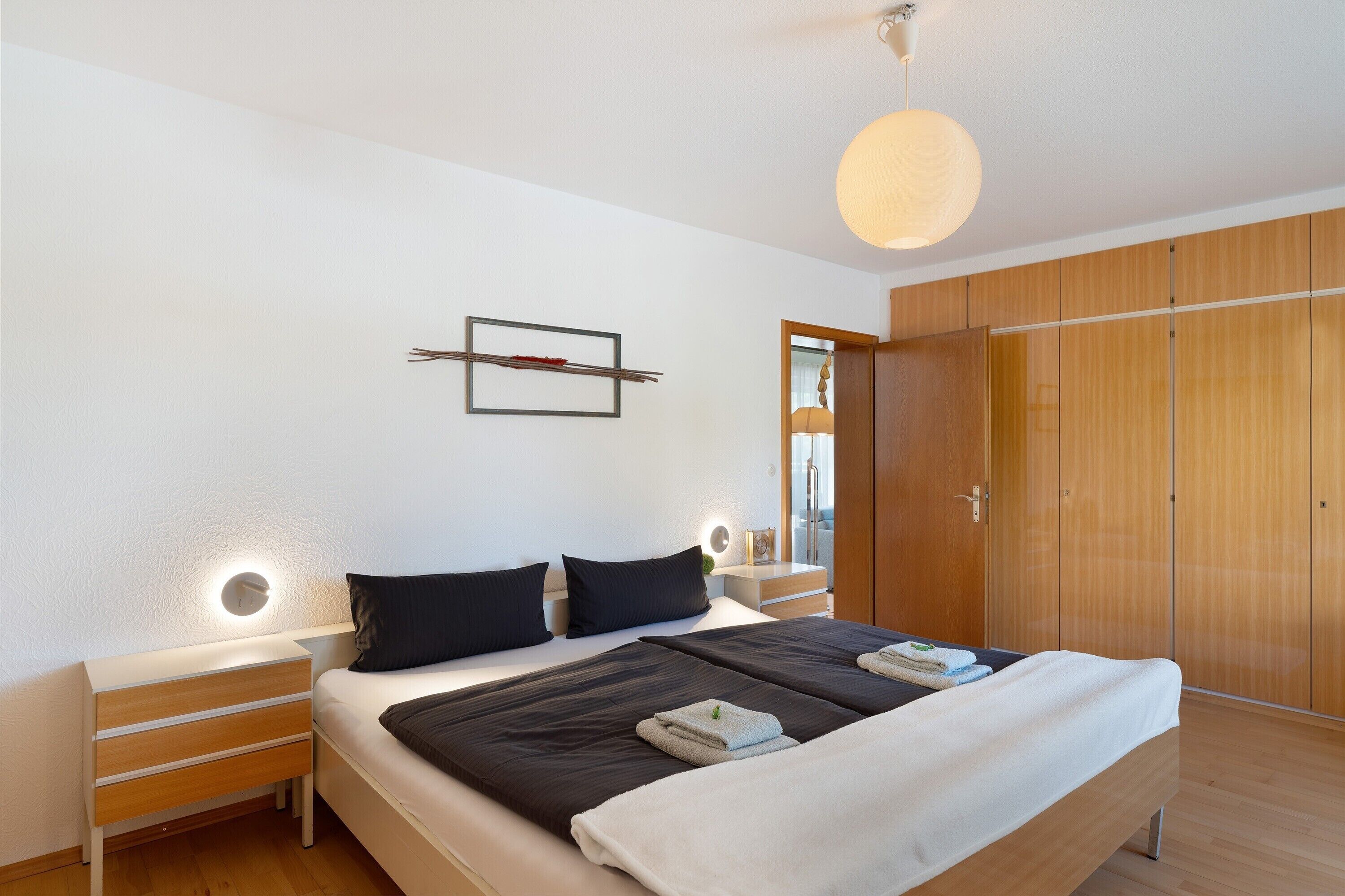 Een moderne slaapkamer met een groot bed, nachtkastjes, een houten garderobe en een wandlamp.