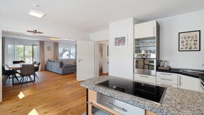 A modern kitchen with an island, white cabinetry, and a dining area with a sofa and table. - Apartment 'Weinbergsuite' with Private Terrace, Balcony and Wi-Fi (Kappelrodeck)