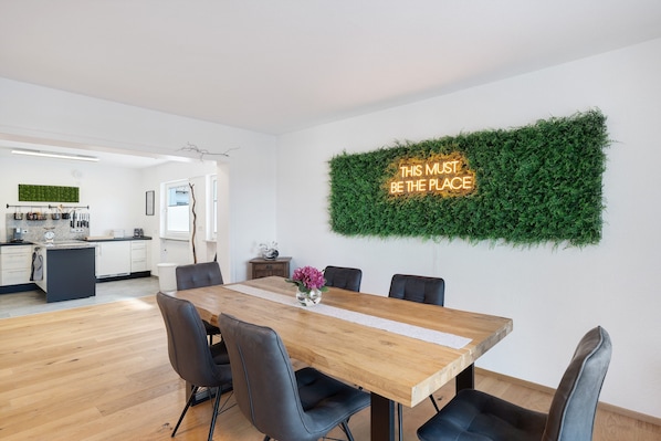 A modern dining area with a wooden table, black chairs, and a neon sign on the wall.
