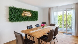 A dining area with a wooden table, six chairs, a neon sign, and a green wall. - Apartment 'Weinbergsuite' with Private Terrace, Balcony and Wi-Fi (Kappelrodeck)