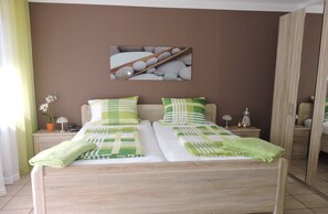 Ein Doppelbett mit grün-weißer Bettwäsche, ein Nachttisch mit Lampe, ein Spiegel und ein an der Wand hängendes Bild.