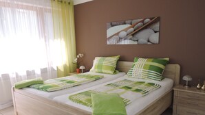Ein Doppelbett mit grün-weißer Bettwäsche, ein Nachttisch mit Lampe und ein Bild an der Wand.