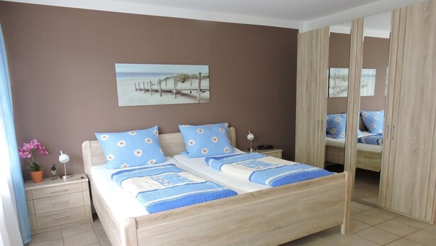 A bedroom with a wooden bed, a nightstand, a mirror, and a beach-themed painting on the wall.