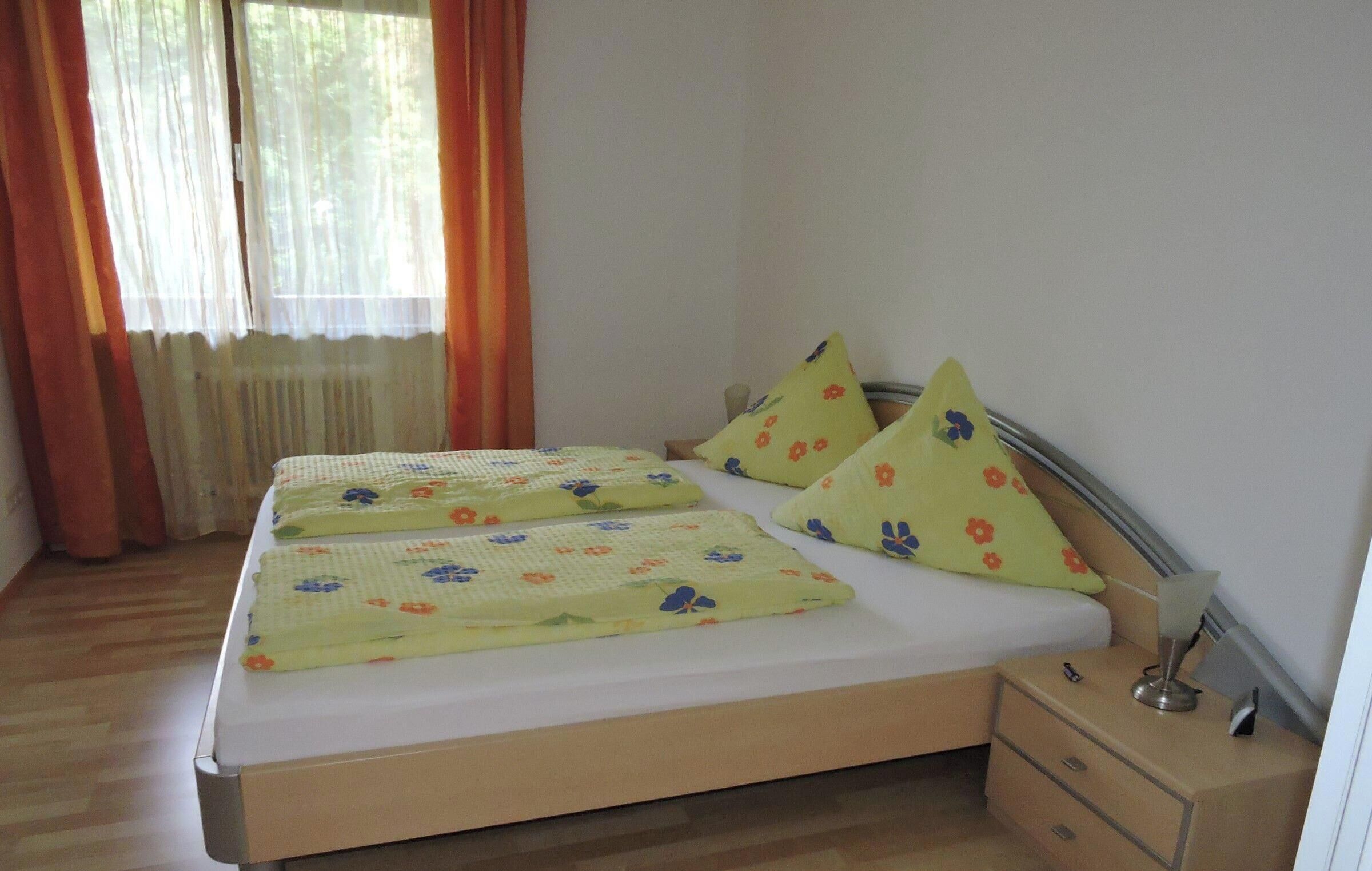 A bed with floral bedding, a bedside table with a lamp, and a window with curtains.