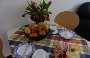 A table with croissants, a vase of tulips, and a cheese platter.