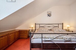 A bedroom with a sloped ceiling, a bed with a metal frame, two bedside tables with lamps, wooden cabinets, and a wall-mounted artwork.