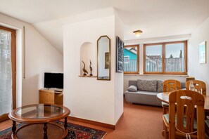A living room with a round glass table, a sofa, a TV, and a dining area with chairs.
