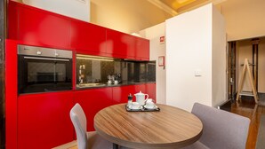 Een moderne keuken met rode kastjes, een ingebouwde oven en een ronde houten tafel met een dienblad vol witte kopjes en een koffiepot.