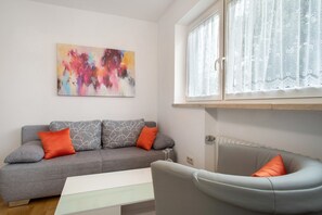 Un salon moderne avec un canapé gris, des coussins orange, une table basse blanche et un tableau abstrait coloré accroché au mur.