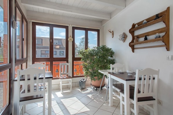 Une terrasse ensoleillée, dotée de meubles blancs, d’une plante en pot et d’une étagère en bois ornée d’objets décoratifs.