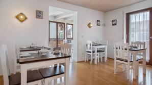 A dining area with white furniture, a wooden ceiling, and a view through an open doorway.