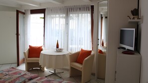 Une pièce avec une télévision, une table, deux chaises et un canapé avec des coussins orange.