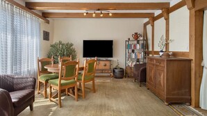 Un salon avec un plafond en bois, un téléviseur à écran plat, une bibliothèque, une table à manger avec des chaises et un canapé.