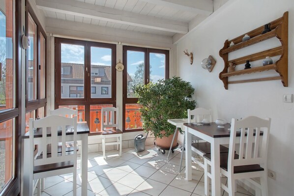 A sunlit patio with white furniture, a potted plant, and a wooden shelf with decorative items.