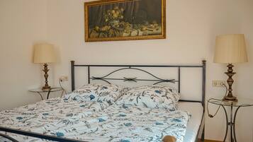 Een bed met een bloemenprint, een schilderij erboven en twee bedlampjes.