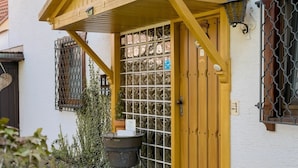 A yellow wooden door with a metal gate, a black pot on a stand, and a small step leading to the entrance.