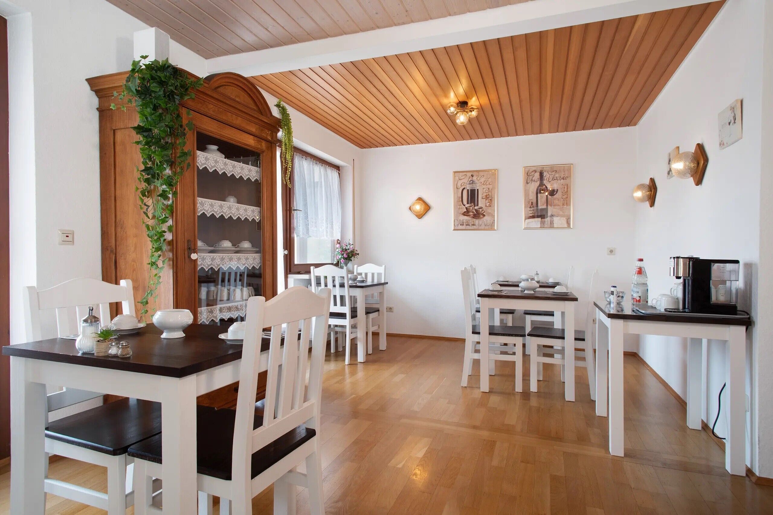 A dining area with white furniture, a wooden ceiling, and wall-mounted light fixtures.