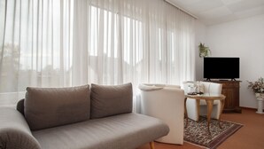 A living room with a sofa, a dining table with chairs, a television, and a potted plant. - Room 'Doppelzimmer 7' with Balcony and Wi-Fi (Wasserburg (Bodensee))