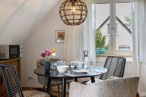 A dining area with a round table, chairs, a hanging light fixture, and a view of a house through a window. - Apartment 'Gute Nacht In Der Acht' with Lake View, Private Garden and Wi-Fi (Überlingen)