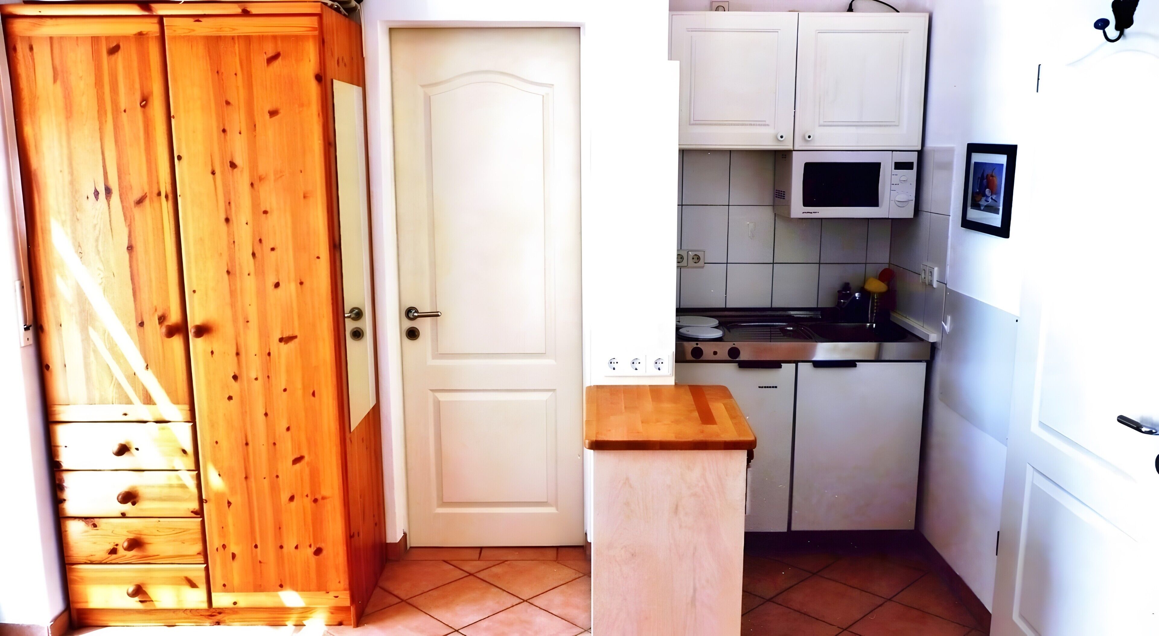 Une cuisine de taille réduite avec des meubles blancs, un four à micro-ondes et une petite table en bois.