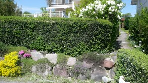 Un barrio residencial con una casa que tiene balcón, un seto bien cuidado y un camino de piedra.