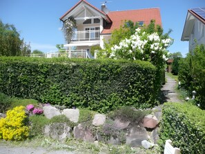 Un quartier résidentiel avec une maison dotée d’un balcon, d’une haie bien entretenue et d’un chemin en pierre.