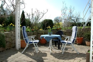 A patio with two striped chairs, a table with a blue tablecloth, and potted plants. - Apartment '2-Zimmer' with Private Terrace, Shared Garden and Wi-Fi (Uhldingen-Mühlhofen)