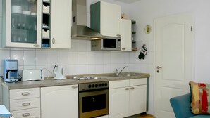 Una cocina con gabinetes blancos, microondas, estufa y cafetera.