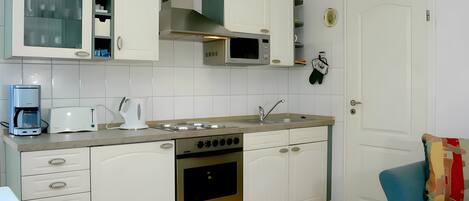 Una cocina con gabinetes blancos, microondas, estufa y cafetera.