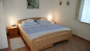 A wooden bed with a blue blanket, two bedside tables with lamps, a small rug, and a painting on the wall.