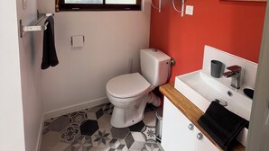 A compact bathroom with a white toilet, a small window, a red wall, and a tiled floor. - Bed and breakfast in Cotentin near shops, beaches and greenway. (Port-Bail-sur-Mer)