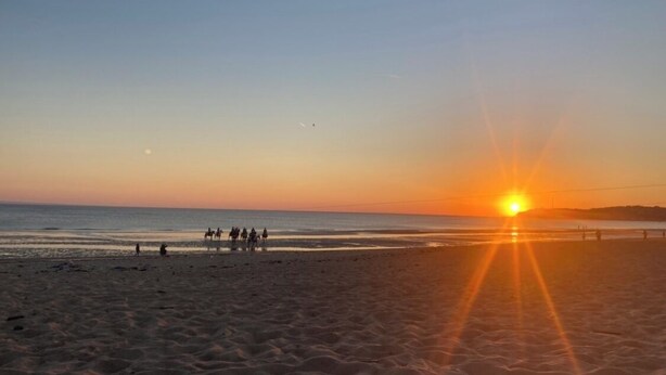 A beach scene with the sun setting over the ocean, people walking, and a clear sky. - Bed and breakfast in Cotentin near shops, beaches and greenway. (Port-Bail-sur-Mer)
