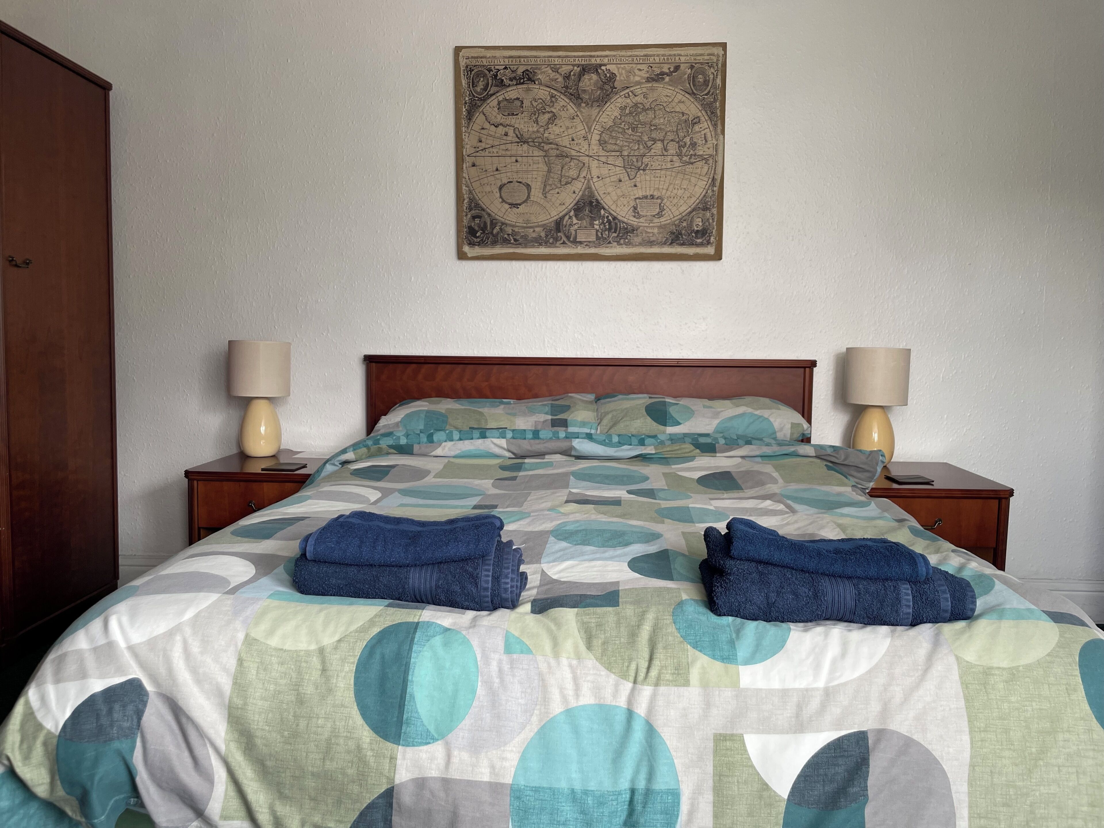 A bedroom with a bed, two bedside tables, a wooden wardrobe, and a wall map.