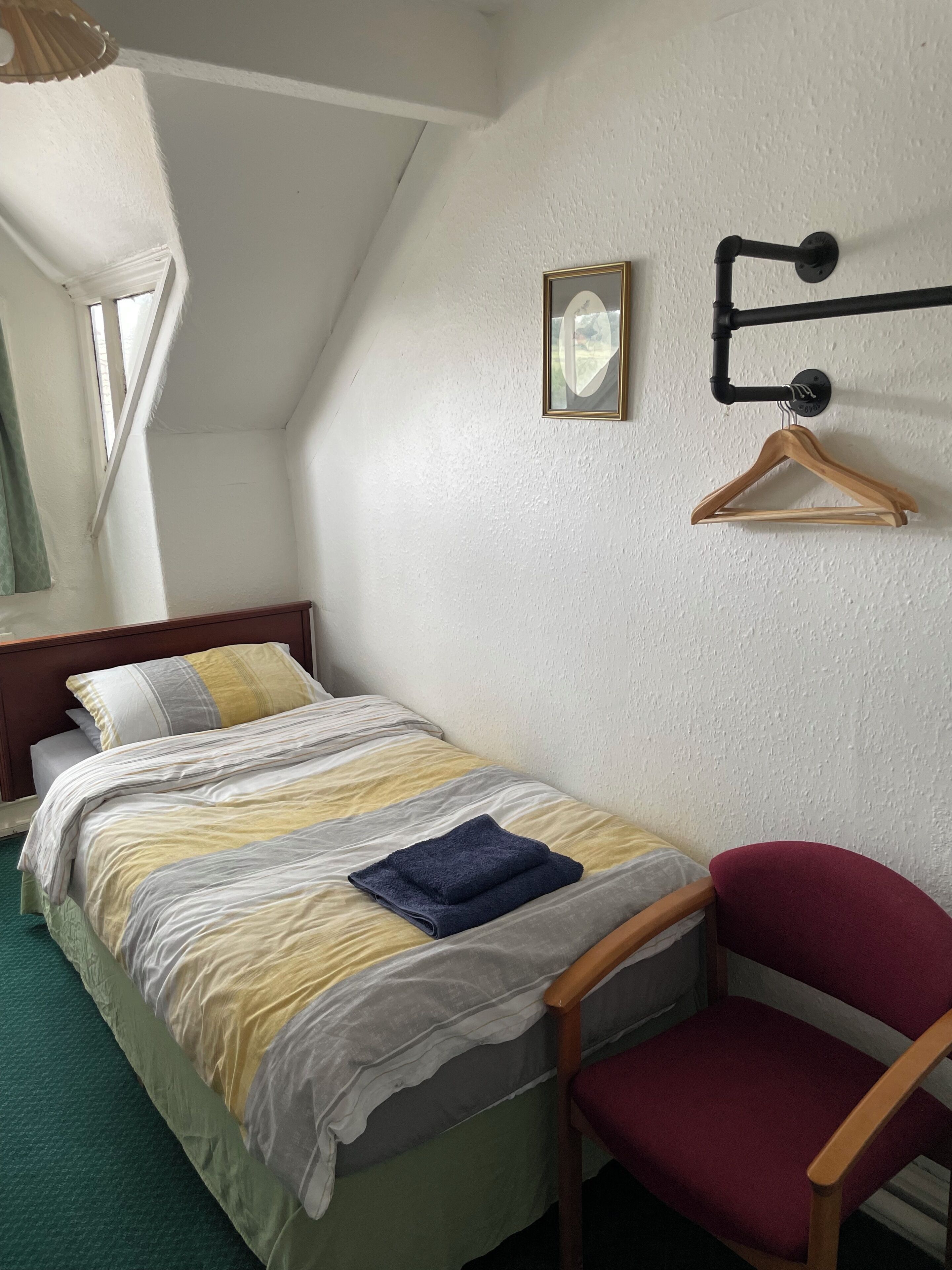 A neatly made bed with a striped bedspread, a blue towel, and a wooden chair with a red cushion.