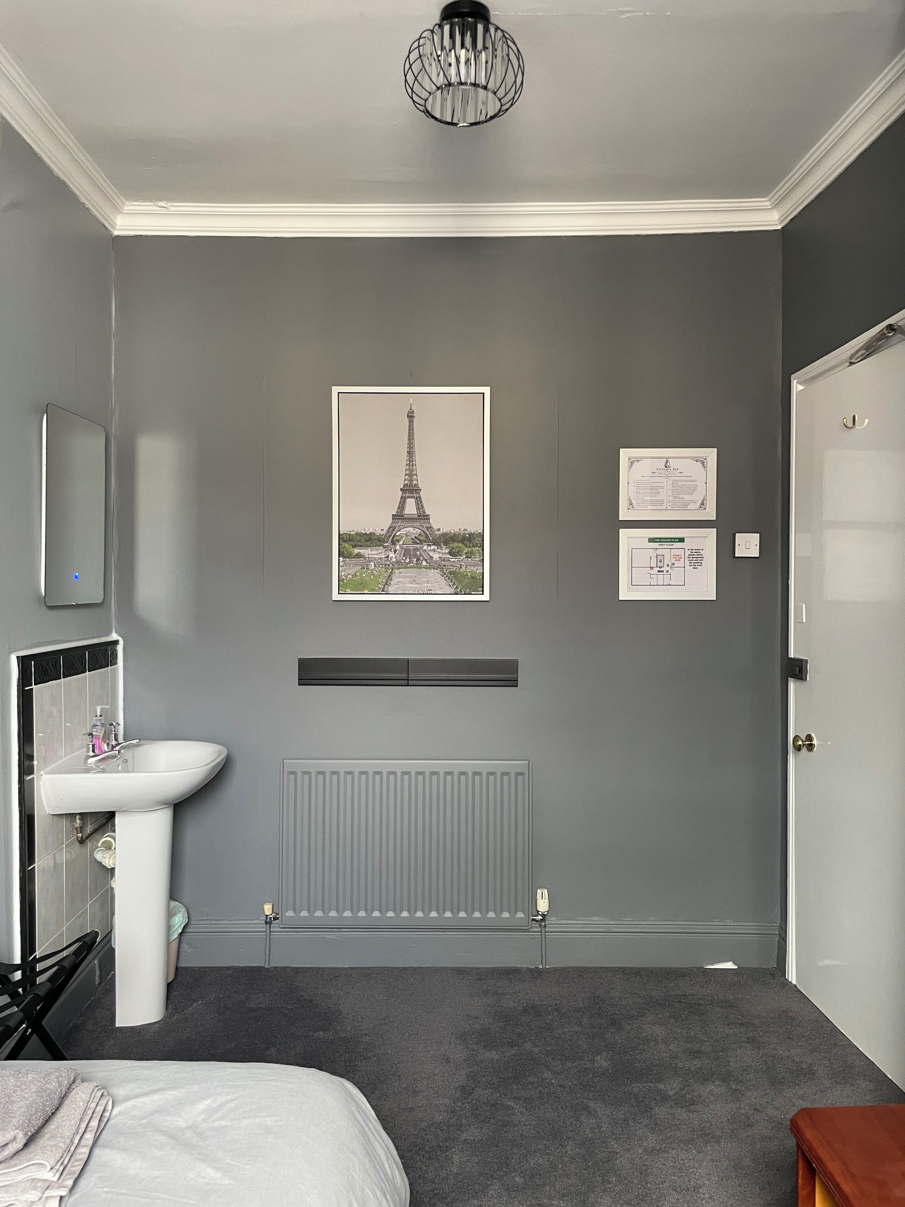 A bedroom with a bed, a radiator, a white sink, a mirror, a door, and a picture of the Eiffel Tower on the wall.