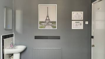A bedroom with a bed, a radiator, a white sink, a mirror, a door, and a picture of the Eiffel Tower on the wall.