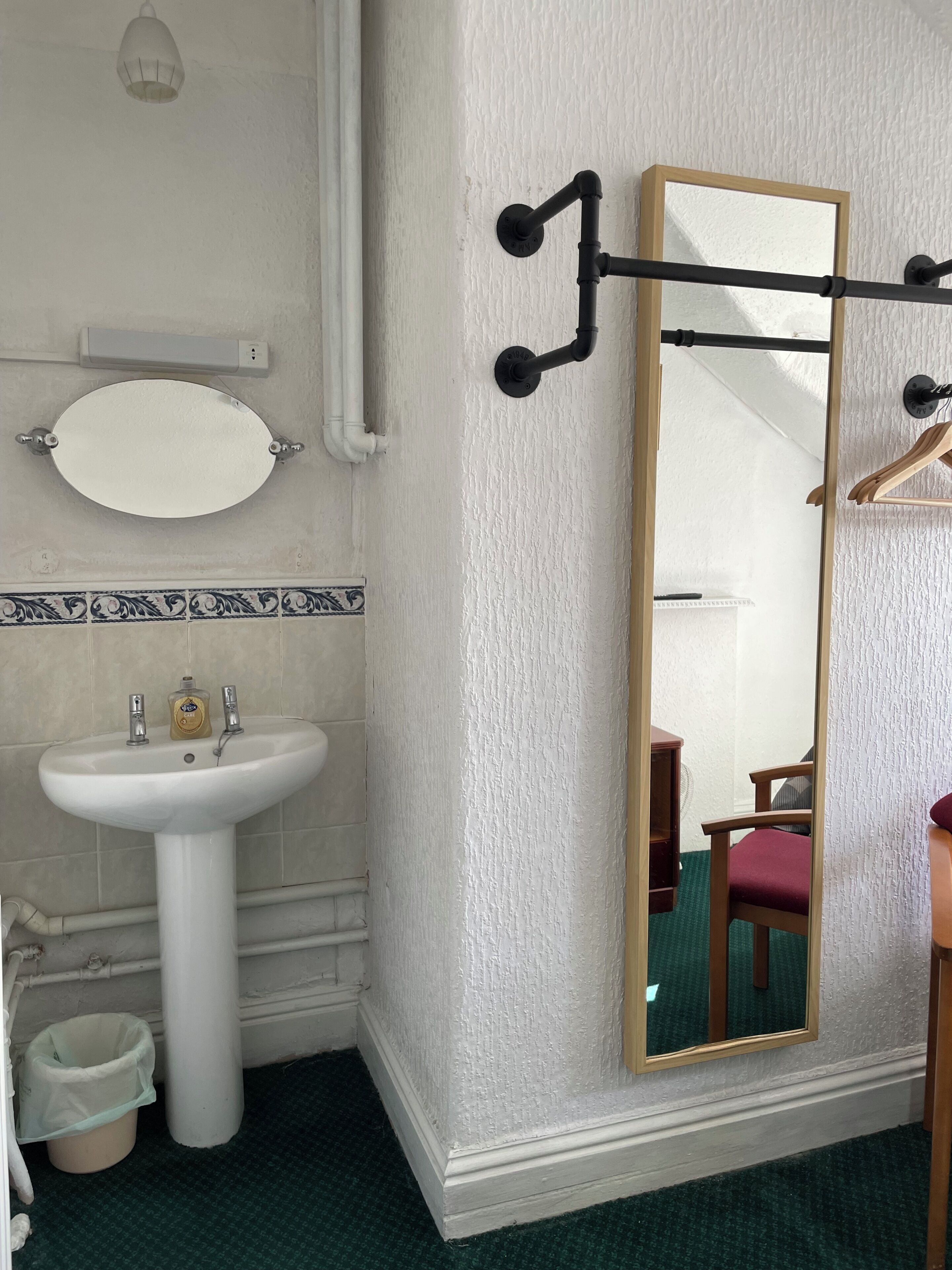 Un baño con un lavamanos blanco, un espejo con marco negro y un perchero para toallas.