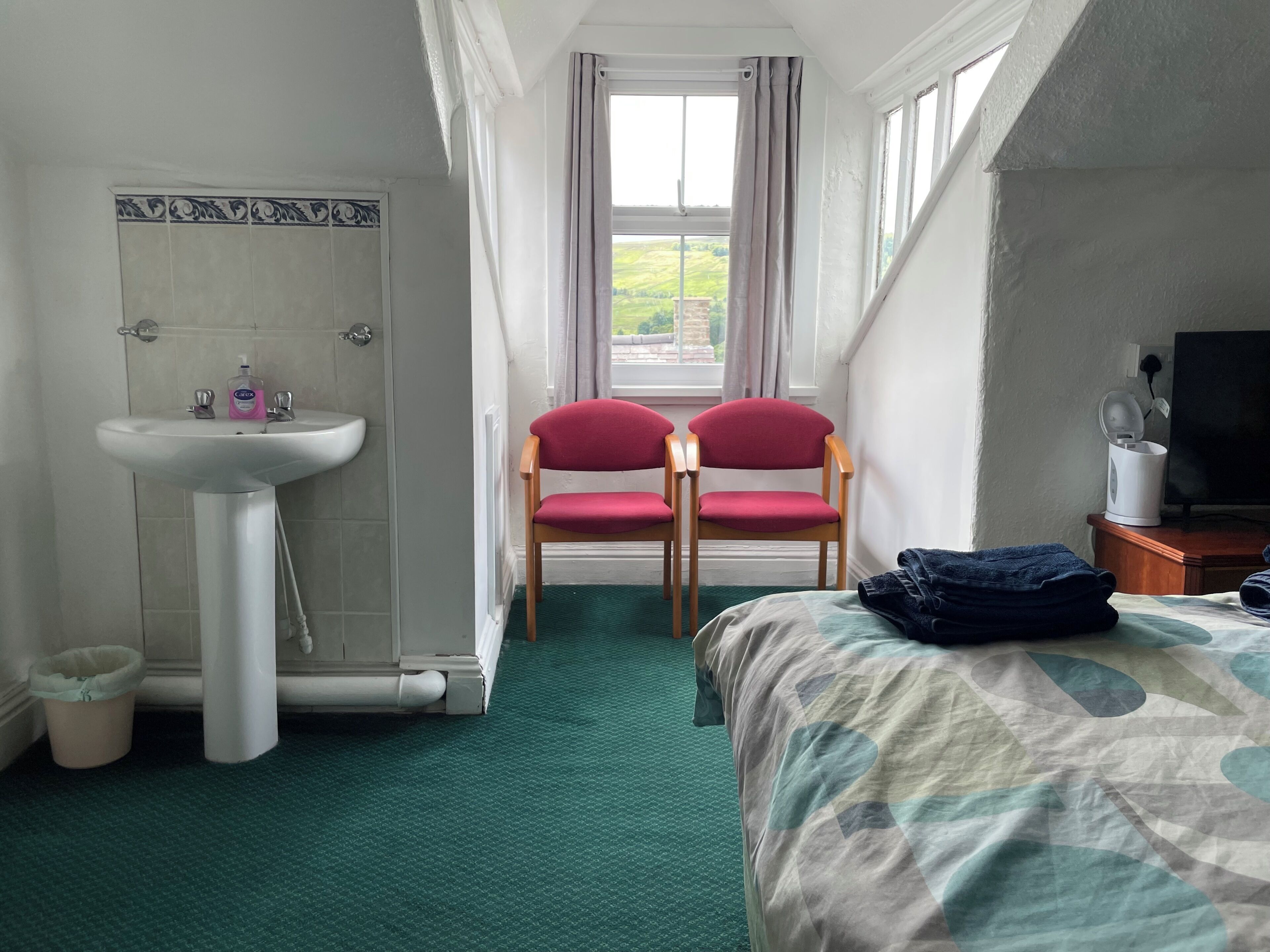 Ein Hotelzimmer mit Bett, Waschbecken, zwei Stühlen, Fernseher und einem Fenster mit Vorhängen.
