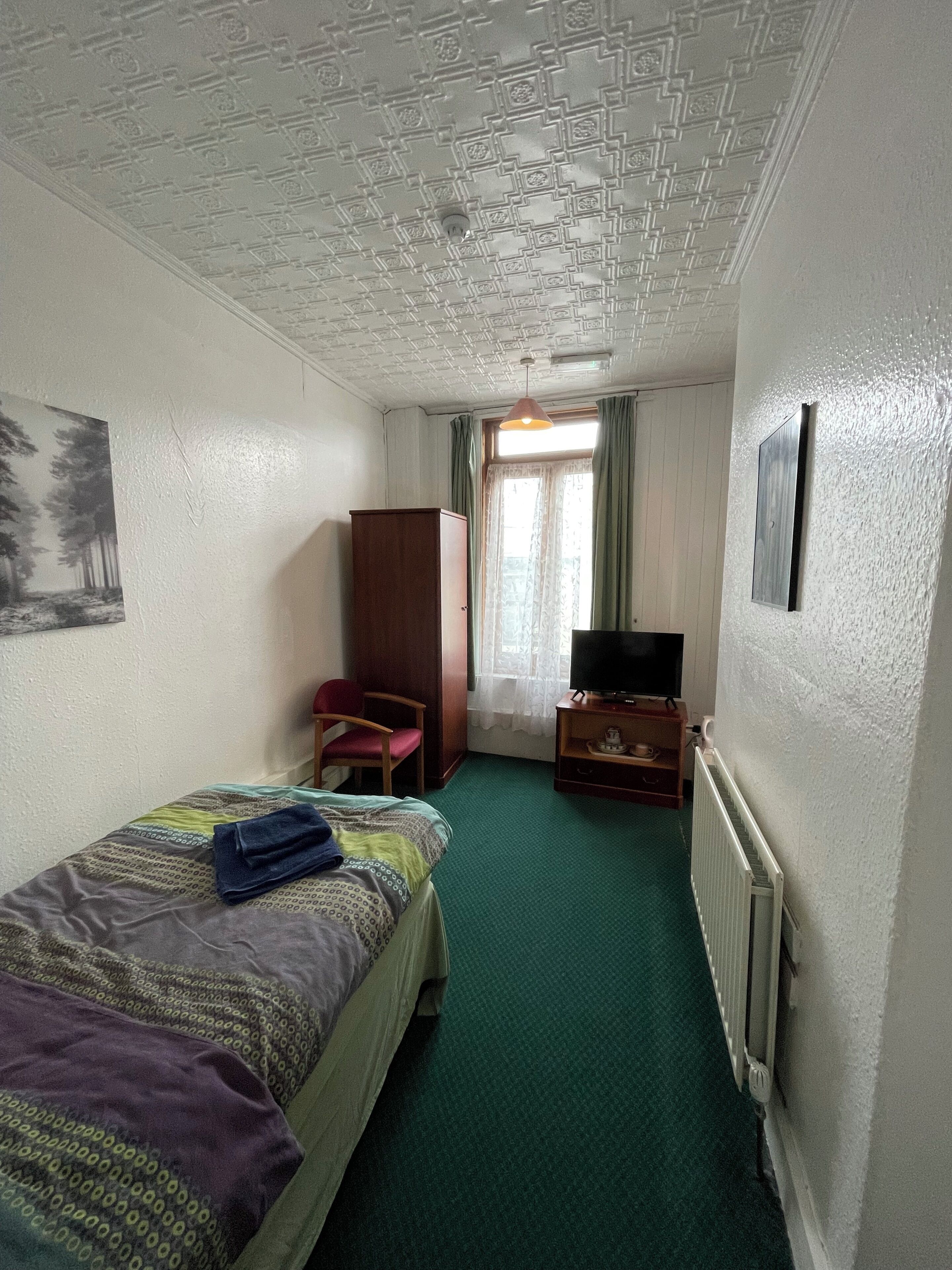 Habitación de hotel con cama, escritorio, silla, televisor, radiador y ventana con cortinas.