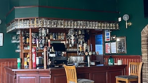 A bar area with a wooden counter, two stools, and a ceiling with a decorative pattern. - Victoria Inn (Alston)