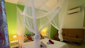 A bedroom with two beds, each with a canopy, a bedside table, and a lamp. - cottages with swimming pool and Spa 900 m from the sea (Sainte-Rose)