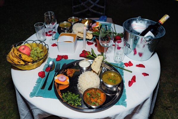 A table set with a variety of dishes, including rice, curry, and bread, along with a bottle of champagne and rose petals.