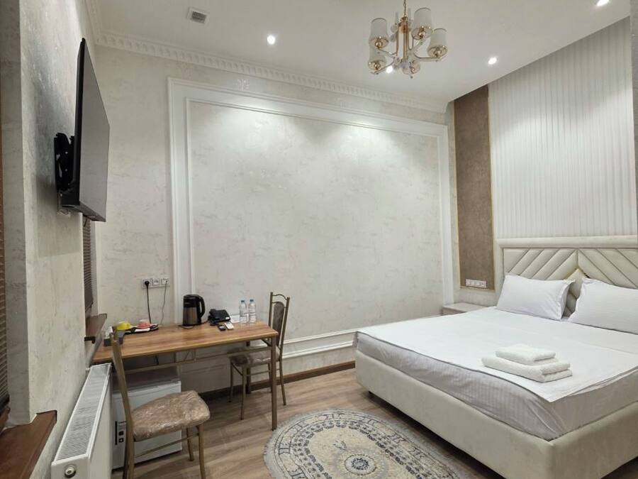 A bedroom with a bed, a desk, a chair, a television, and a ceiling light.