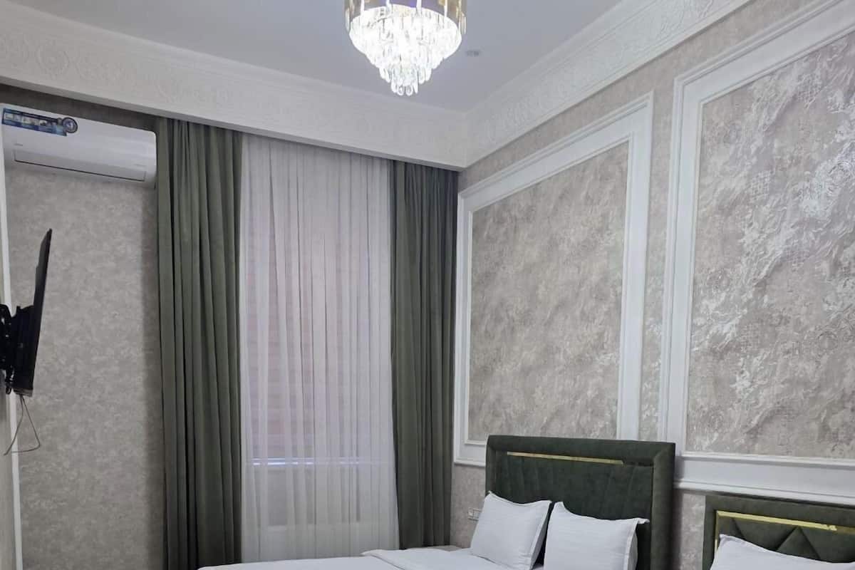A hotel room with two beds, a chandelier, a television, and a window with curtains.