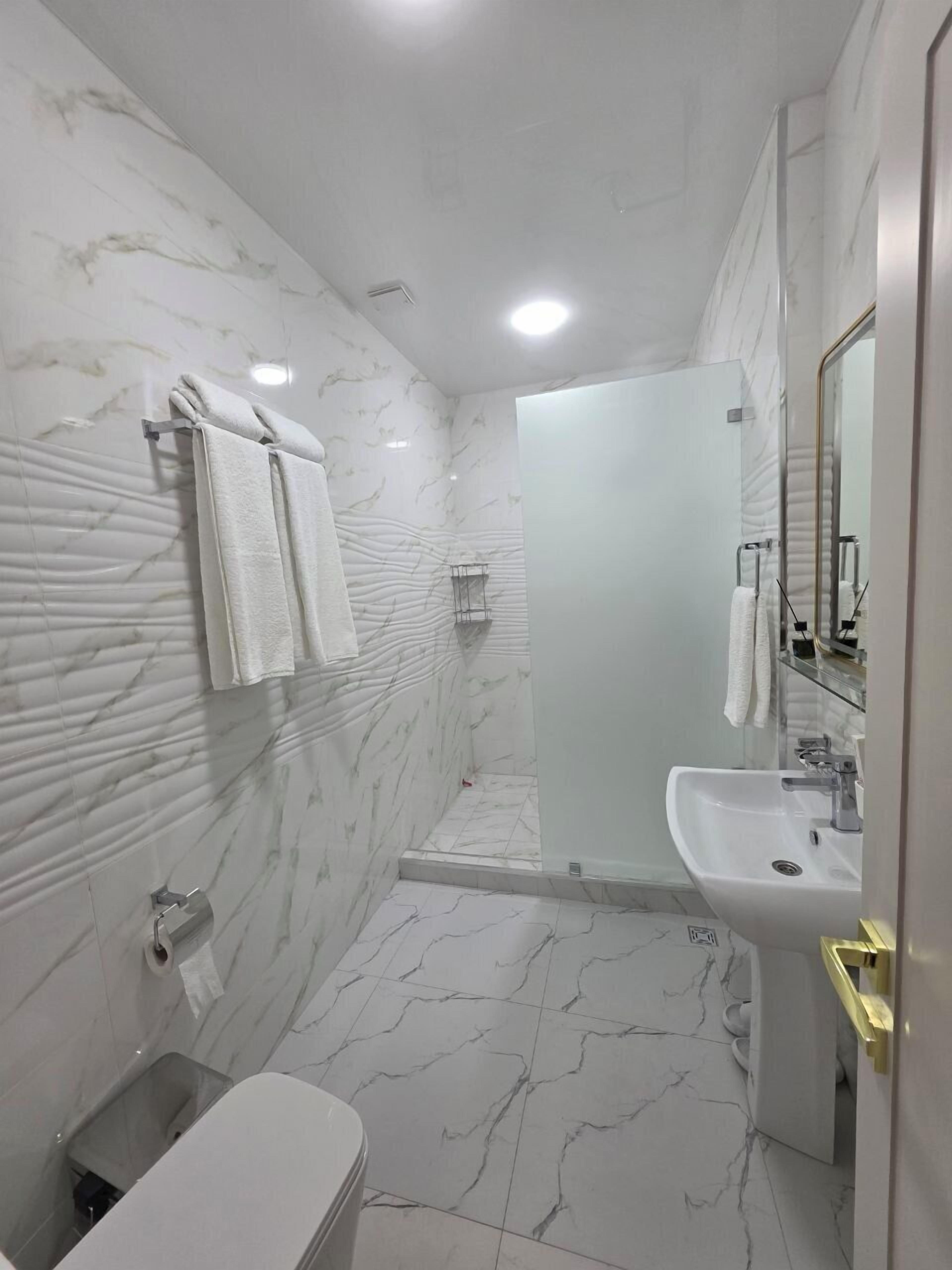 A bathroom with marble walls, a toilet, a sink, and a shower area.