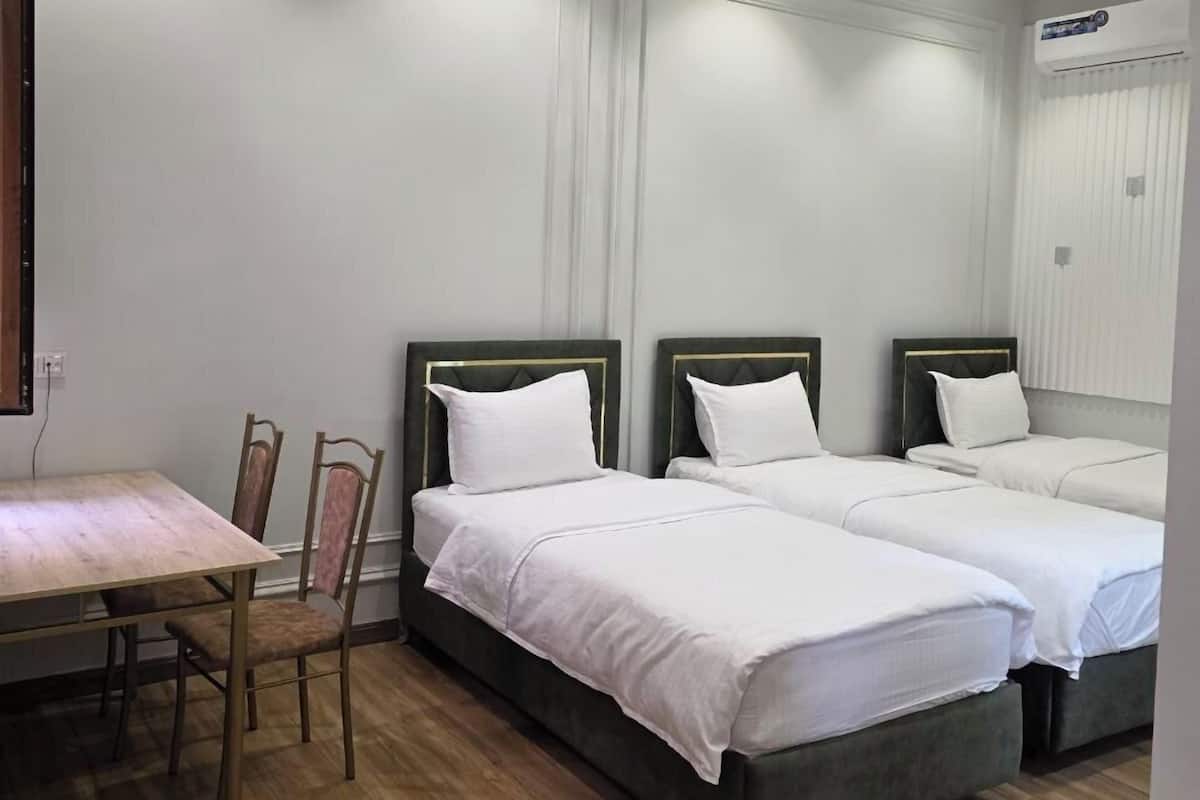 A hotel room with two beds, a wooden dining table, and a ceiling fan.