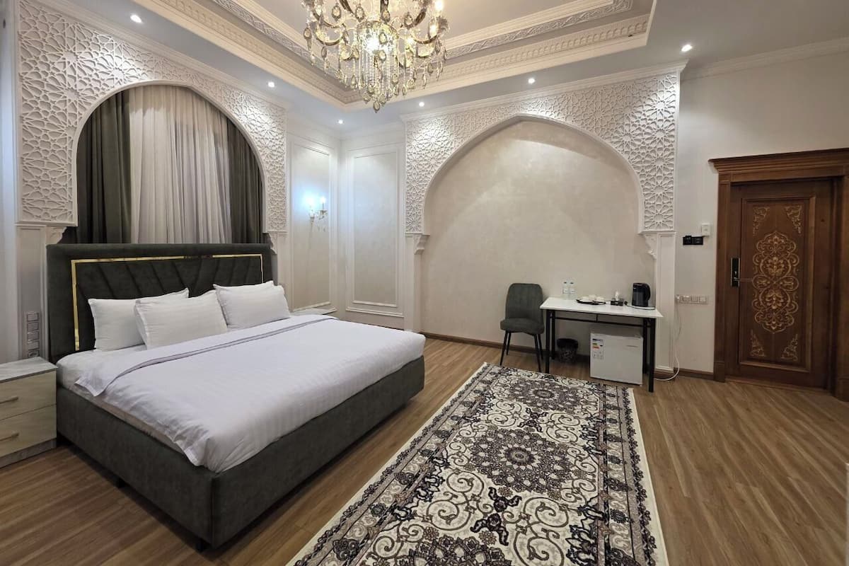 A bedroom with a bed, desk, chair, and a chandelier.