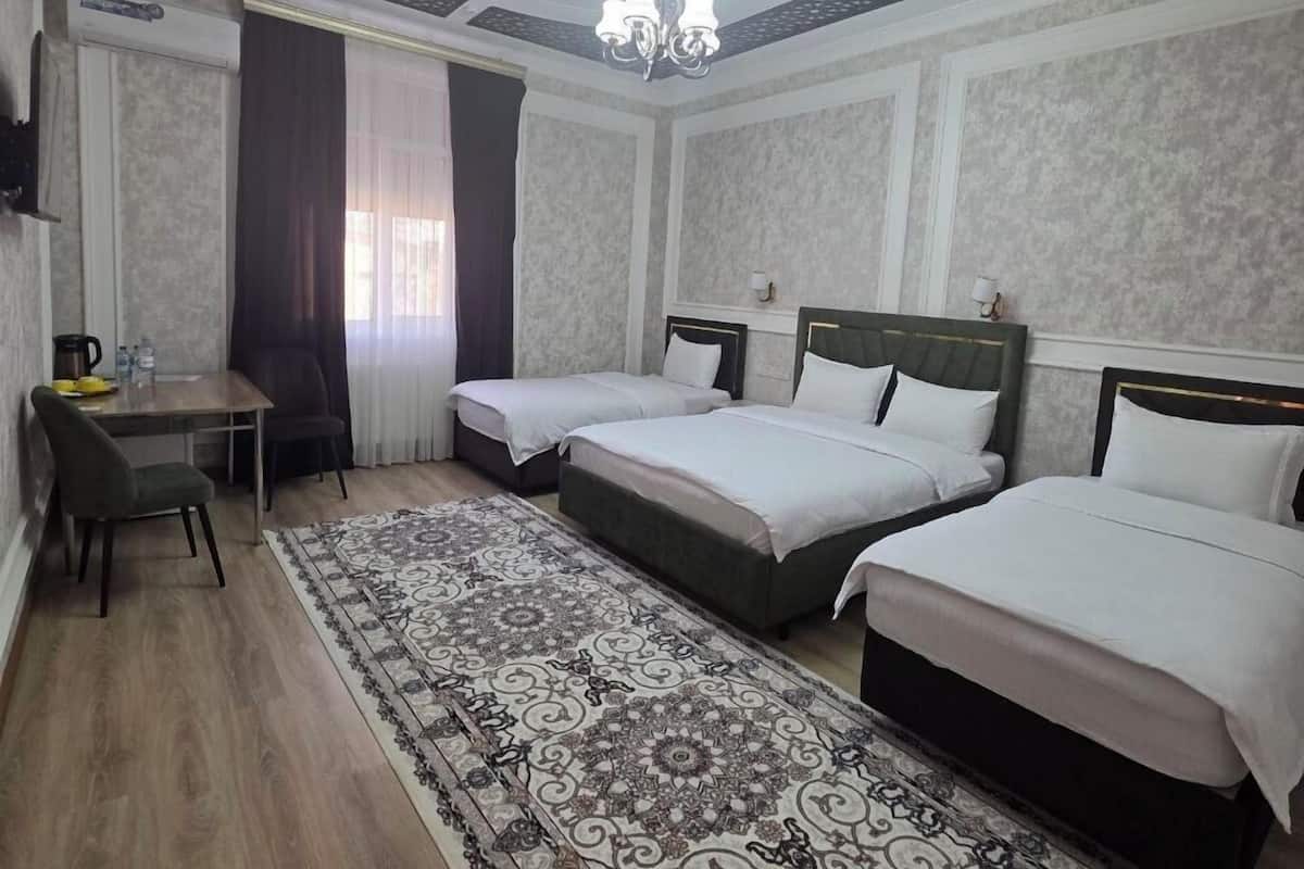 A hotel room with two beds, a desk, a chair, a patterned rug, and a chandelier.