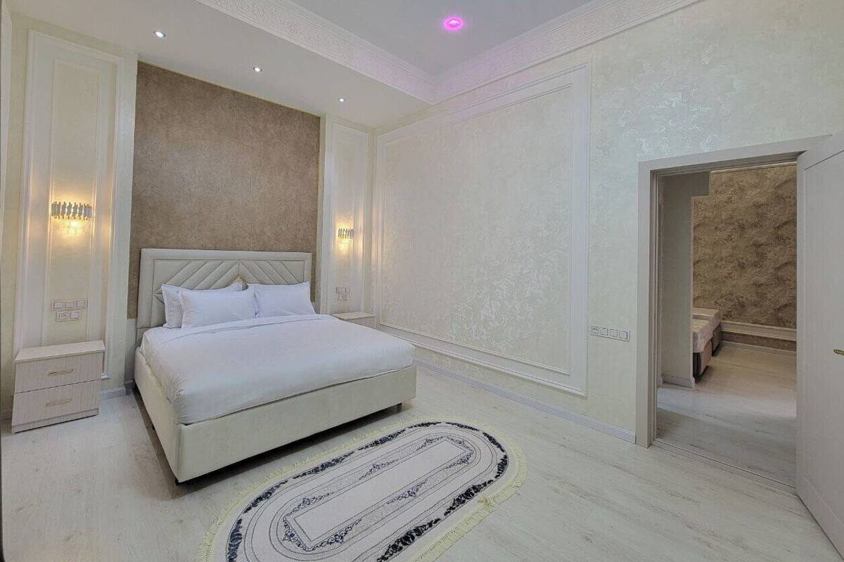 A spacious bedroom with a large bed, a chandelier, and a view into another room.